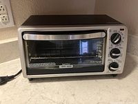 Front view of Black & Decker toaster oven on countertop showing control knobs and glass door.