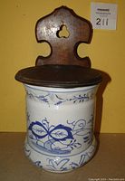 Front view of porcelain salt box with blue floral design and wooden backing and lid.