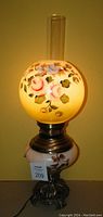 Frontal photo of the antique electrified lamp showing the hand painted glass globe with roses and other flowers, base with floral design, brass fittings and ornate metal base.
