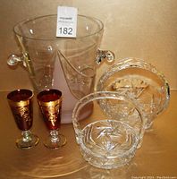 Photo of all lot items: large cut crystal vase with handles, two cut crystal baskets with cut design, two ruby colored aperitif glasses with gold detailing.