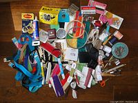 Photo of assorted vintage and new sewing notions spread on a wooden surface, showing zippers, pins, needles, thread spools, elastic bands, embroidery hoops, hooks & eyes, bias tape and small sewing accessories.