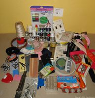 Wide view showing entire sewing notions lot with threads, zippers, elastic bands, bias tape, scissors, pin cushions, needles, and other sewing accessories arranged on table.