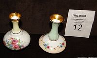 Two miniature bone china vases side by side on dark background, showing floral decoration and gold-rimmed necks.