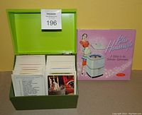 Green Betty Crocker recipe box open showing stacks of recipe cards inside alongside the 'Retro Housewife' book with pink cover and vintage illustration