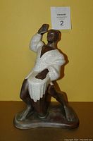 Front view of the ceramic Hawaiian dancer figurine with drum, showing the figure kneeling with one arm raised and wearing a white textured garment.