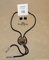 Full lot showing black braided bolo tie with horseshoe stone pendant, gold-tone horse and horseshoe tie clip, and black onyx cuff links