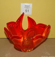 Front view of orange art glass dish showing flame-like sculpted edge details and translucent gradient color from orange to amber at base