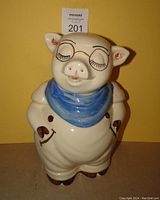 Front view of vintage Shawnee pig cookie jar showing smiling face with closed eyes, original glasses with clear glaze, blue bandana, and painted details.