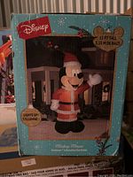 Box of 11 ft tall inflatable Mickey Mouse dressed as Santa Claus. The box shows an image of the inflatable lit up outside a house decorated for Christmas.