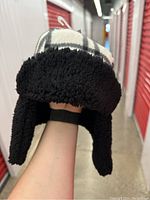 Front view of a trap style winter hat showing black sherpa fleece ear flaps and black and white plaid pattern on top and front.