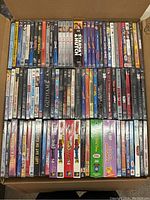 Wide view of top two rows of DVDs in cardboard box, shows mix of TV series, movies and children’s titles