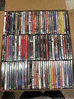 Full view of DVDs stacked in box showing various TV series and movie titles including Suits, The Flash, Gotham, Arrow, etc.