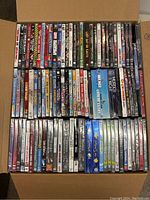 Box filled with approximately 96 new DVDs in original packaging, showing a range of titles and genres.