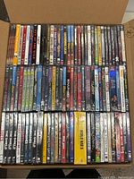 Top-down view of opened cardboard box filled with rows of DVD cases, showing spines of multiple titles.