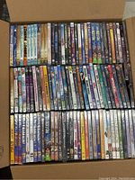 Box filled with approximately 99 DVD cases arranged in rows, visible titles include Losers, Redline, The Lucky One, and several animated titles.