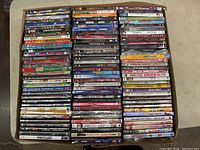 Top view of box showing approximately 80 DVDs in used condition with varying titles and cases, some worn and damaged.