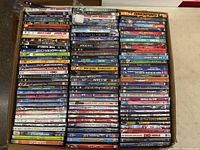 Overview photo of a box filled with many DVD cases stacked tightly, showing covers and spines with visible wear and tear
