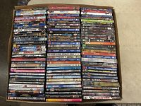 Photo showing approximately 45 DVD cases stacked side by side with visible titles including Tremors Anthology, Two and a Half Men, Prancer, Homeland, Code Black, and others.