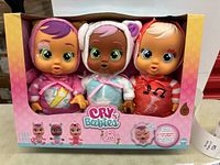 Front view of the boxed set of three Cry Babies Tiny Cuddles dolls showing each doll's unique outfit and facial features in original packaging.