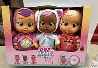 Front view of boxed set showing 3 dolls in cute animal themed hooded outfits, colors pink, teal, and red, labeled Cry Babies Tiny Cuddles