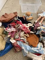 Photo showing assortment of antique doll clothing in various colors and fabrics, including bonnets and dresses