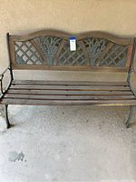Iron and wooden outdoor bench showing front view with floral and lattice designed backrest. Condition is used with visible dirt.