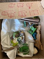 Box containing multiple frog figurines including a metal frog with tools and ceramic frog figures