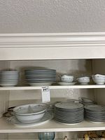 Shelves of Noritake china showing stacks of dinner plates, dessert plates, and divided bowls with floral pattern and silver trim.