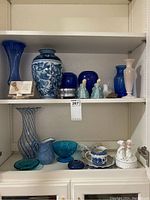 Shelf displaying a variety of glassware items including cobalt blue vases, turquoise bowl, pink vase, and ceramic figurines.