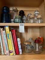Cookbooks and various glass jars with cork and screw lids inside wooden cabinet shelf