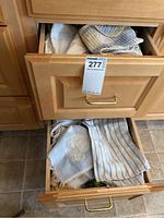 Two open wooden kitchen drawers filled with various dish towels and washcloths, showing different colors and patterns including stripes, checks, florals, and solid colors