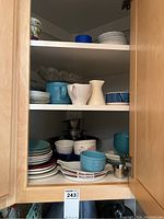 Cabinet shelves with assorted dishes such as plates, bowls, mugs, and saucers in various colors and styles