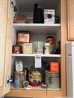 Kitchen cabinet with top and middle shelves containing a black French press, several boxed teas, loose tea containers, vintage tins, and other kitchen items.