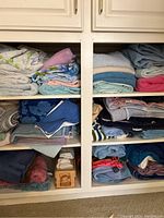 View of linen closet shelves holding assorted folded linens such as towels, bath rugs, sheets or blankets in various colors and patterns.