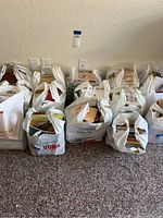 Fifteen plastic bags lined up against a wall, filled with books, showing variety in size and cover design.