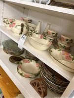 Multiple shelves showing an assortment of Franciscan Earthware china in a floral rosebud pattern, including bowls, plates, cups, and a sugar bowl. Also some decorative plates in different colors.