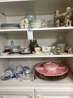 Shelves filled with assorted mini tea cups, saucers, various dishes, serving trays and ceramic figurines including a pottery jug and bird sculptures.