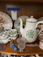 Porcelain teapot with spout, cups, saucers, blue horse figurine, glass vase, and other porcelain and glass items on shelf
