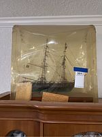 Plastic encased ship model displayed on top of a cabinet, showing full ship with rigging and rig details alongside attached two typed historical papers.