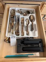 Drawer containing various silverware items organized in a white tray, along with a black foam maker device and blue chopsticks.
