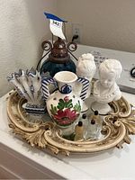 Overall shot of the lot showing the ornate gilded mirror base, stained glass lamp, two ceramic vases, two white bust figurines, and two small glass bottles.