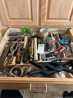 Drawer with various tools including screwdrivers, files, pliers, chisels, hand saw, measuring tape, clamps, and packaging of small parts