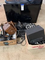 Full view of the Samsung TV with two boxes filled with electronic items including cables, remotes, and small devices.