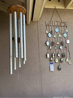 Aluminum tube wind chime with wooden top hanging against wall.