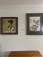 Photo showing two framed pictures hung on a white wall: an Asian floral art print with calligraphy and a portrait of a mother and child.