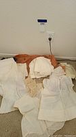 Photo showing multiple vintage white and off-white baby dresses, knit socks/booties, and crocheted scarves arranged on carpet.