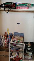 Full view showing several rolls of wrapping paper standing upright next to a basket filled with ribbons and other supplies, along with reusable bags on the floor and shelf above