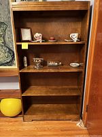 Full frontal image of the solid wood bookcase showing four shelves, detail on top frame, and medium brown finish. Items on shelves not included.