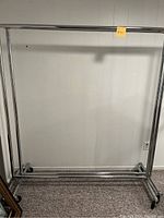 Full front view of one metal clothing rack against a wall showing wide rectangular frame and wheels.
