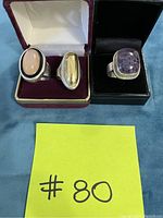 Three silver rings displayed in open boxes on blue fabric background with yellow lot card #80 in front.
